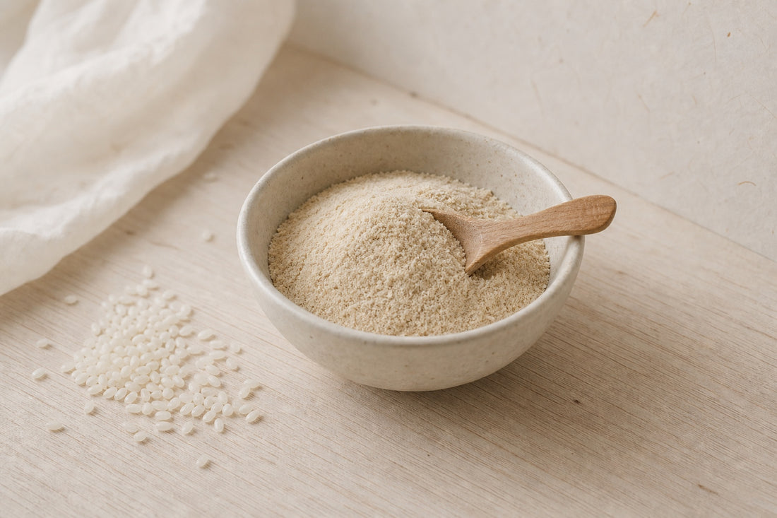 Rice bran powder in a ceramic bowl with a wooden scoop and scattered rice grains