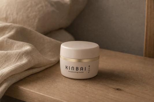 Kinbai Moisturizing Cream jar on a bedside table with folded linen in warm evening light