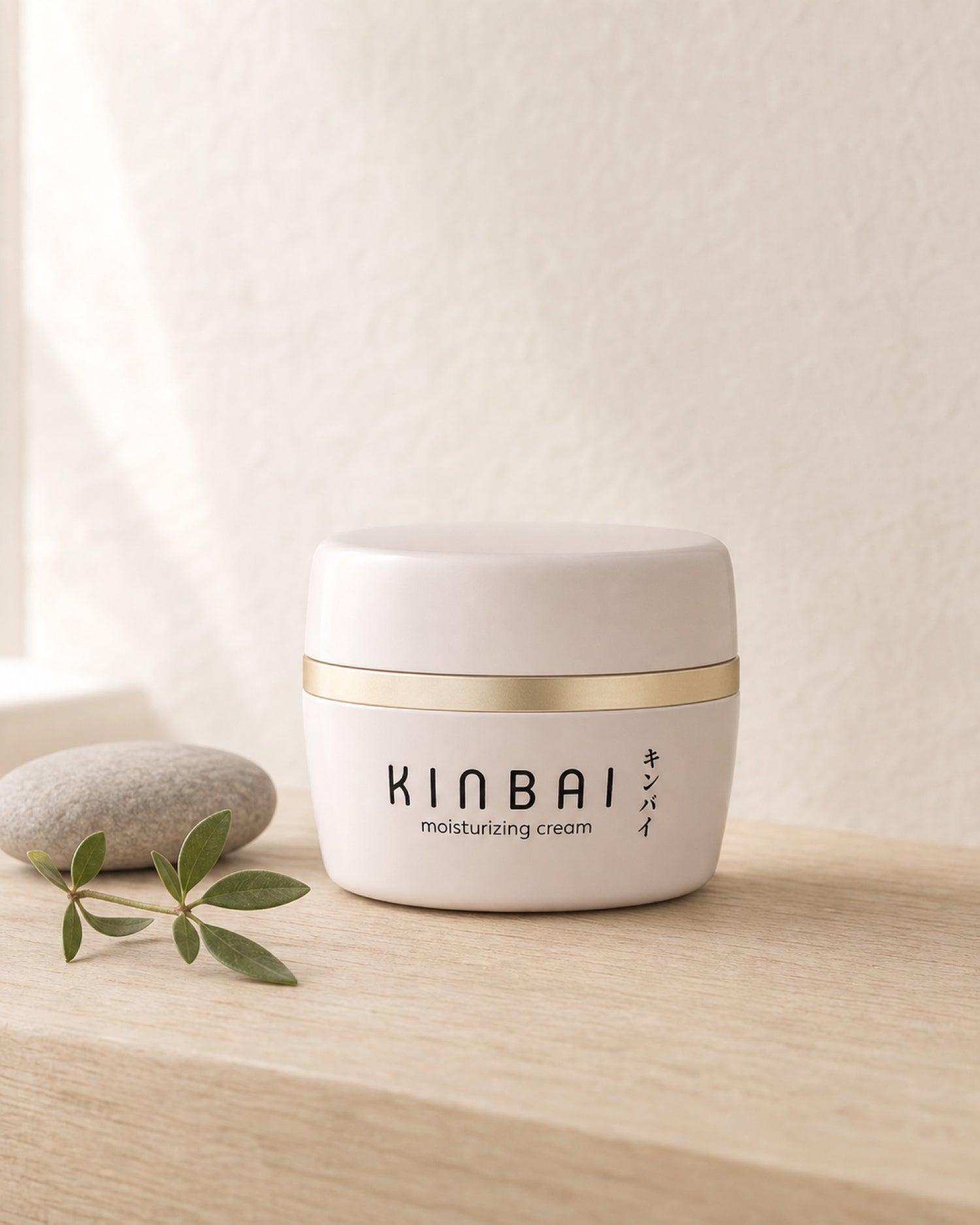 Kinbai Moisturizing Cream jar on pale wood by a bright window with a smooth stone and green sprig